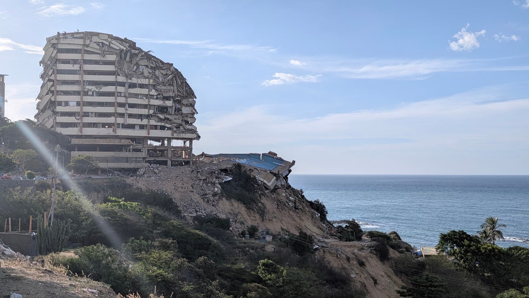 Un edificio residencial de varios pisos, colapsado y colgando sobre el borde de un acantilado frente al mar en La Guaira.