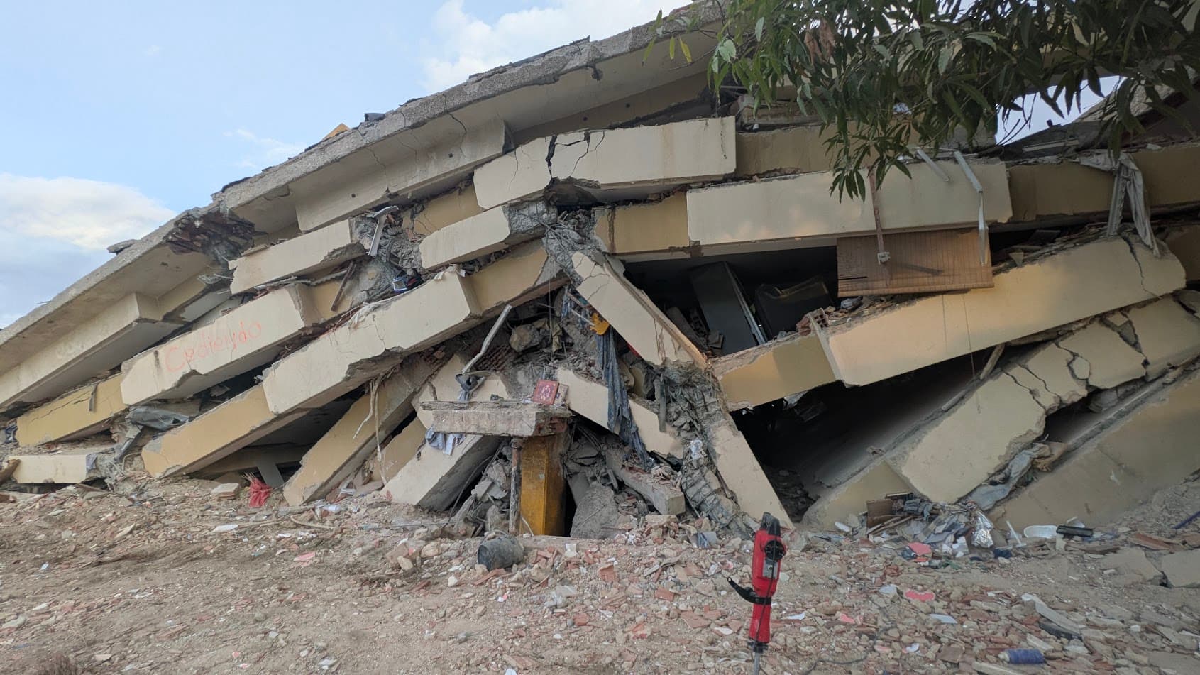 Vista cercana de una estructura de concreto colapsada, con los pisos apilados unos sobre otros tras el derrumbe.